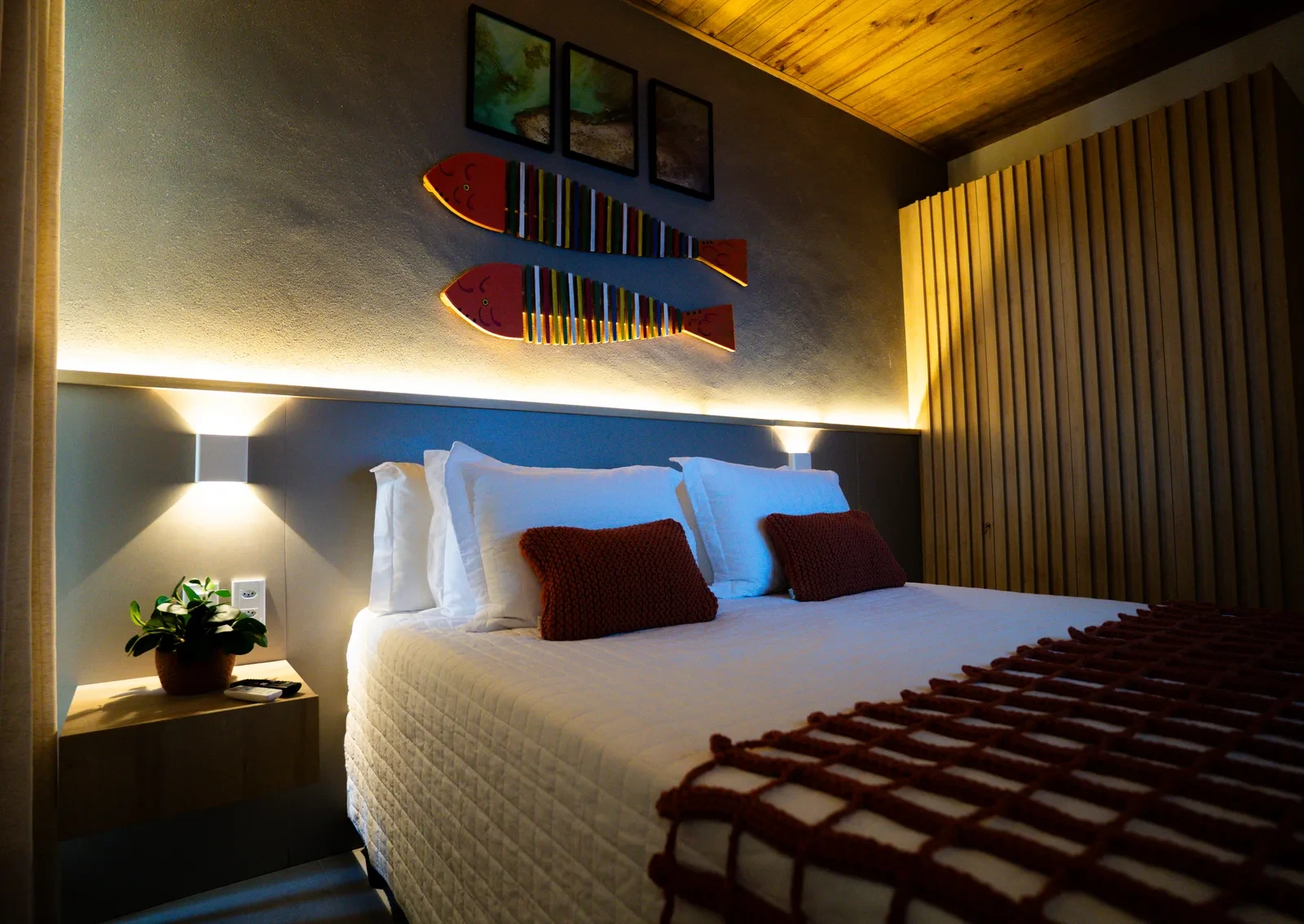 Suíte com cama box Queen, cabeceira ripada e luminárias de leitura.